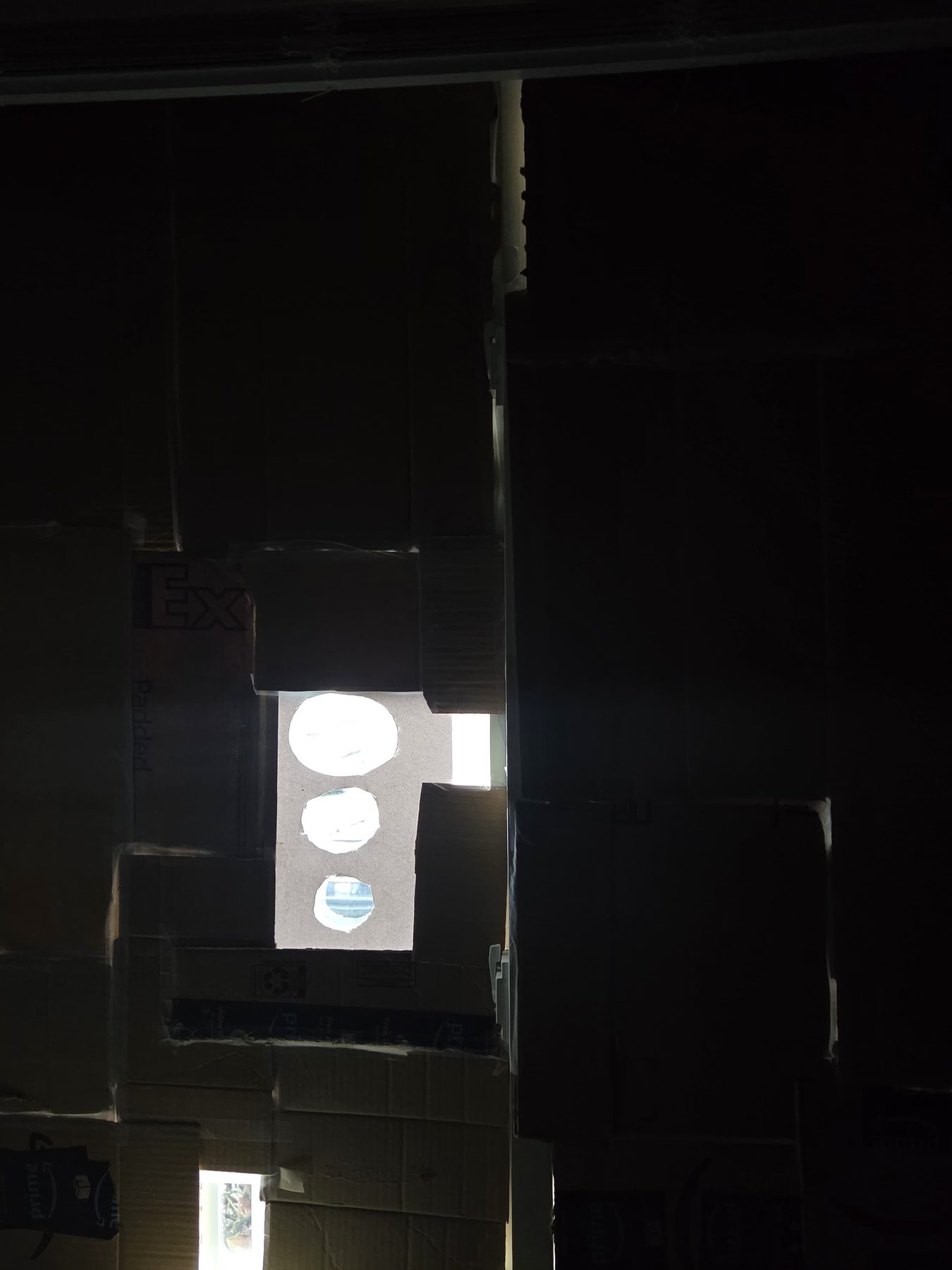 A window covered in cardboard, three small holes letting light through